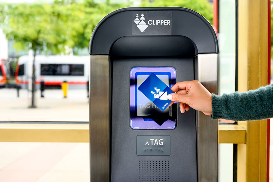 Close-up of a person's hand holding a plastic Clipper card in front of a standing Clipper card reader.