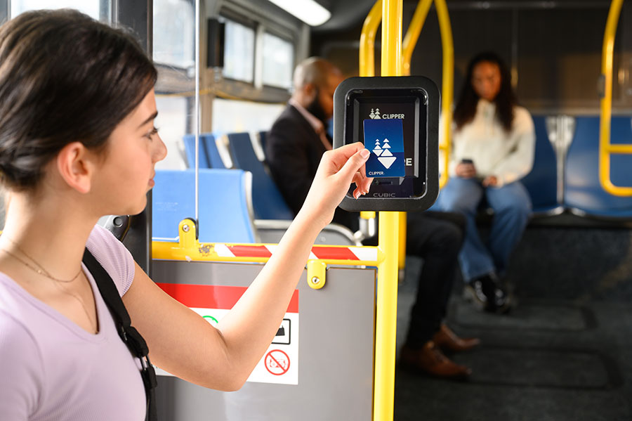 A youth boards a bus, holding up a plastic Clipper card to a bus card reader.