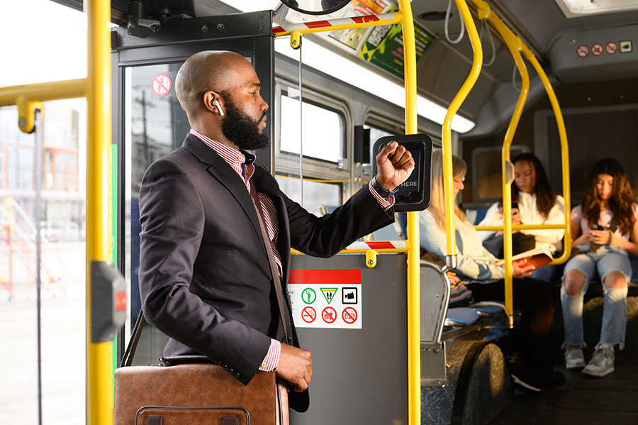 An adult boards a bus, holding their wrist with an Apple Watch up to the Clipper card reader to pay with a mobile Clipper card.